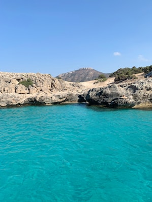 blue sea beside brown rocky mountain under blue sky during daytime