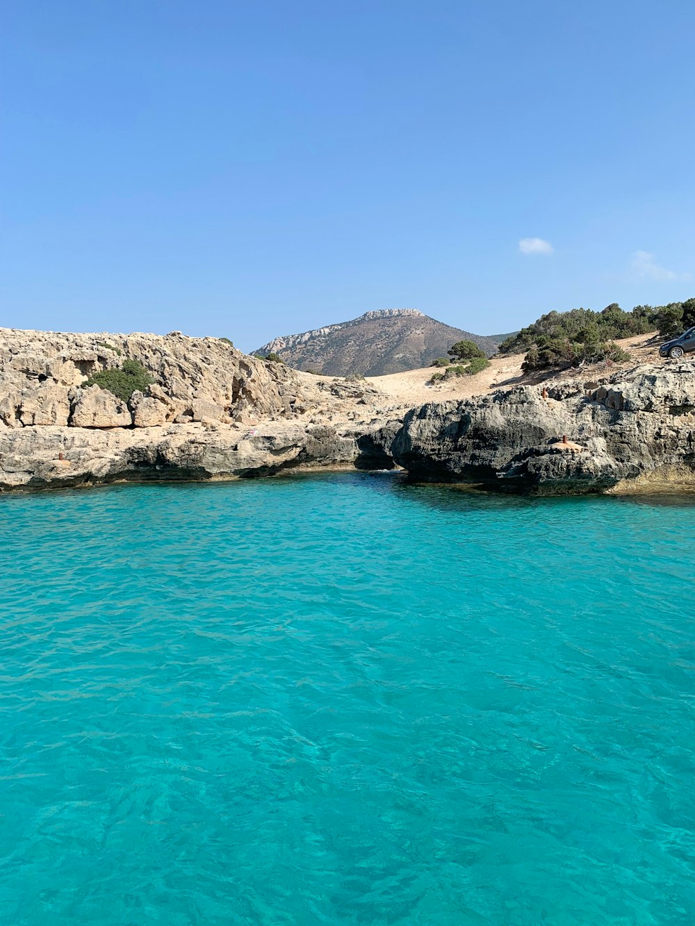 blue sea beside brown rocky mountain under blue sky during daytime