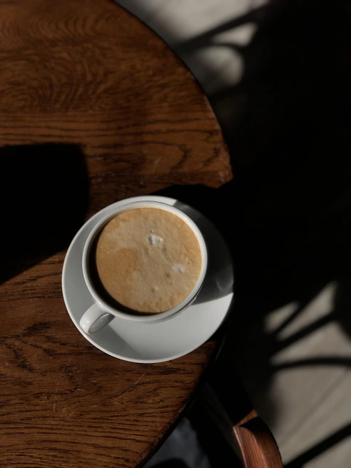A sleek stainless steel travel cup resting on a wooden table with morning sunlight.