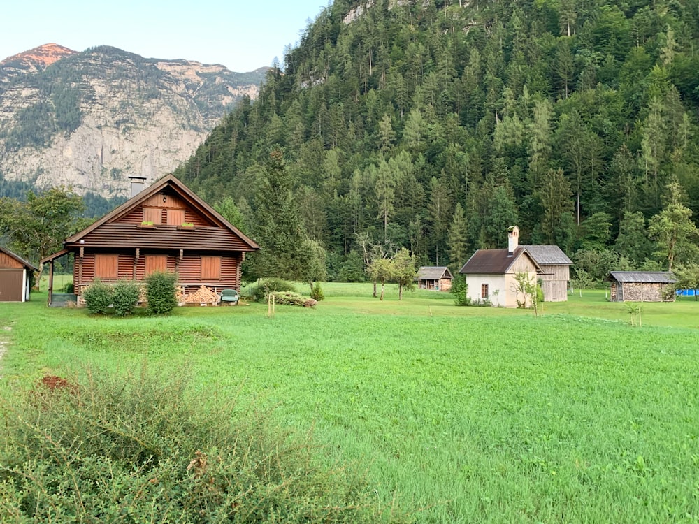 casa de madeira marrom no campo de grama verde perto da montanha verde durante o dia