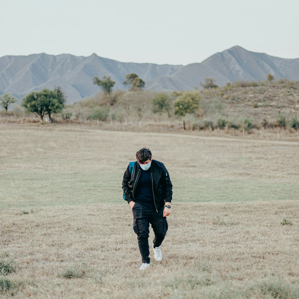 uomo in giacca nera che cammina sul campo di erba verde durante il giorno