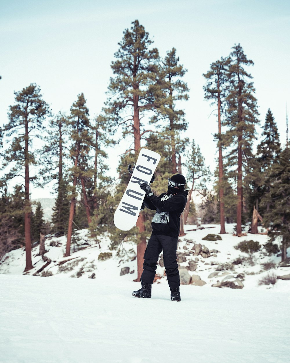 man in black jacket and black pants carrying white and black snowboard on snow covered ground