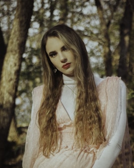 woman in white and orange long sleeve shirt standing near brown tree during daytime