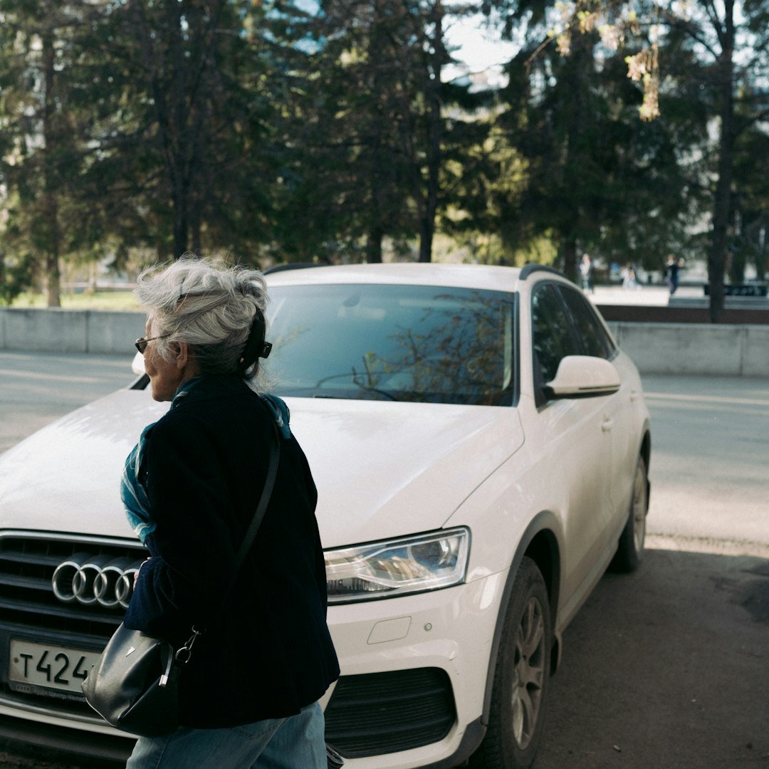 woman in black jacket standing beside white audi car during daytime