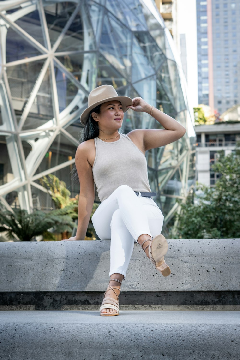 woman in white tank top and white pants sitting on concrete bench during daytime