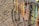 Colorful handmade necklaces and bracelets hang from a metal frame next to a sandy beach. The frame is part of an old bicycle wheel, and the strands vary in color, including vibrant yellows, oranges, pinks, and blues.