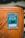 A collectible card encased in a protective sleeve is displayed on a wooden surface. The card features a blue and white illustration of a powerful creature labeled 'Obelisk the Tormentor'. The card text includes details about the creature's attributes such as attack and defense points.