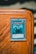 A collectible card encased in a protective sleeve is displayed on a wooden surface. The card features a blue and white illustration of a powerful creature labeled 'Obelisk the Tormentor'. The card text includes details about the creature's attributes such as attack and defense points.