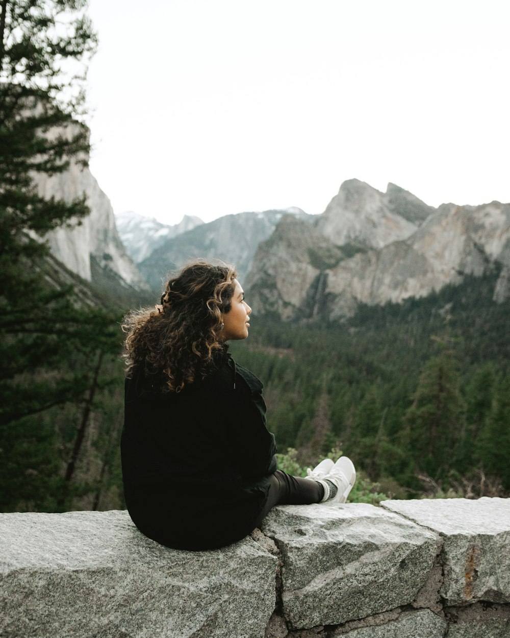 Frau in schwarzem Langarmhemd sitzt tagsüber auf Felsen in der Nähe des Sees