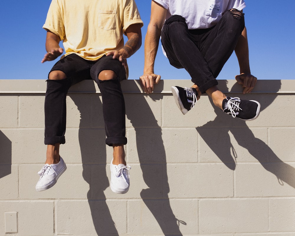 man in yellow shirt and black pants sitting on white concrete wall