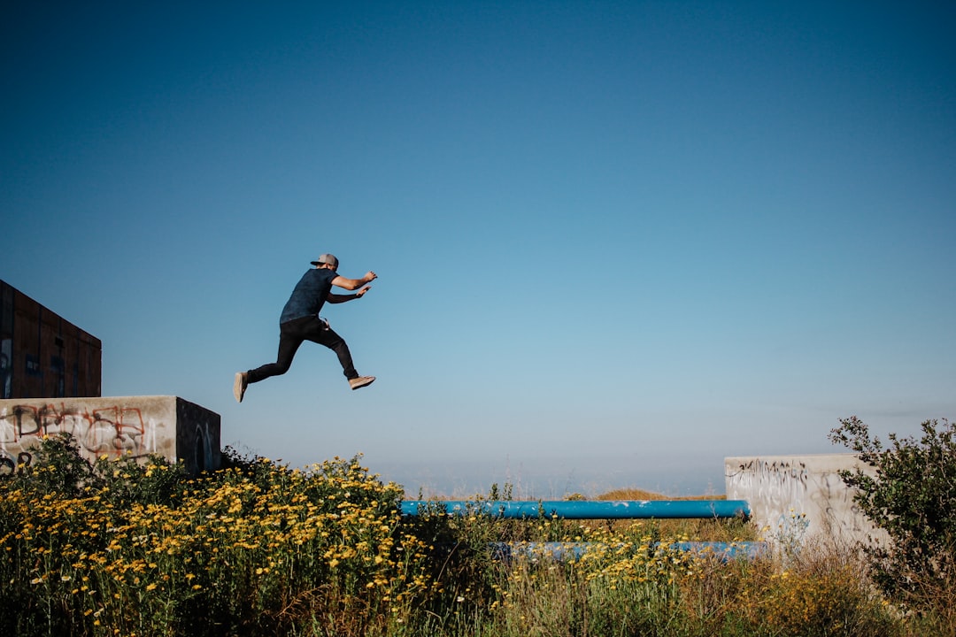 man in black t-shirt and black shorts jumping on brown wooden fence during daytime