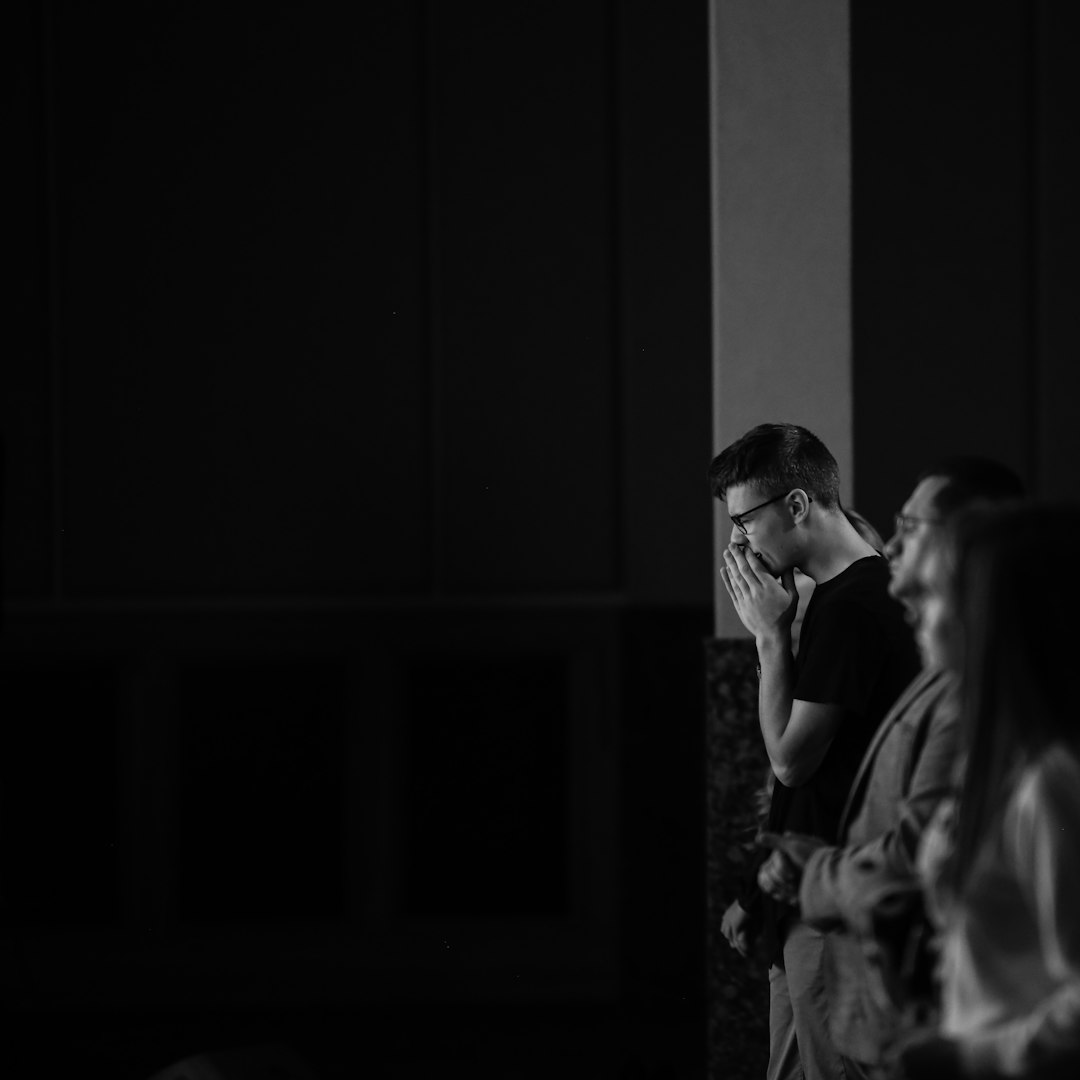 grayscale photo of man and woman standing near window