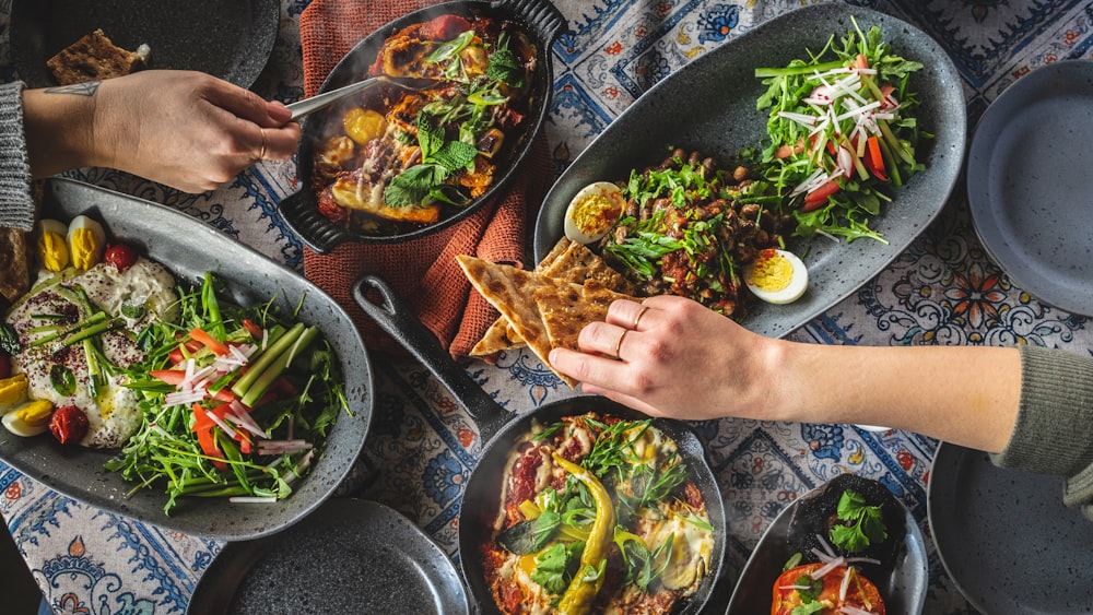 person holding vegetable salad on black ceramic plate