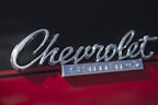 Chrome 'Chevrolet Camaro' emblem mounted on the exterior of a car. The background features a glossy surface with a red and black color scheme.