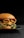 A gourmet hamburger is placed on a black plate, featuring layers of melted cheese, crispy bacon, fresh green lettuce, and a succulent beef patty, all encased in a glossy brioche bun. The background is dark, highlighting the appetizing colors and textures of the burger.