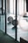 A gym setting with a barbell loaded with weights placed on the floor. The background shows gym equipment such as rings and possibly weightlifting platforms. Lighting appears to be natural, coming through large windows.