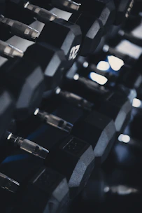 Close-up of heavy dumbbells aligned on a rack under soft, dramatic lighting in a fitness studio.