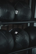 Several black weighted medicine balls are stacked on a rack, each labeled with a number indicating their weight.
