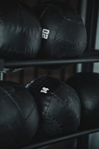 Several black weighted medicine balls are stacked on a rack, each labeled with a number indicating their weight.