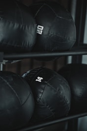 Several black weighted medicine balls are stacked on a rack, each labeled with a number indicating their weight.