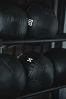 Several black weighted medicine balls are stacked on a rack, each labeled with a number indicating their weight.