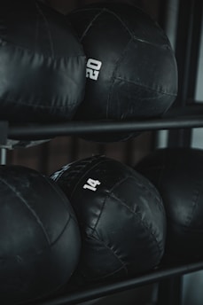 Several black weighted medicine balls are stacked on a rack, each labeled with a number indicating their weight.