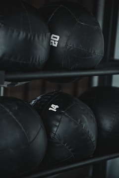 Several black weighted medicine balls are stacked on a rack, each labeled with a number indicating their weight.