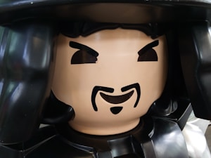 A large, detailed plastic figurine resembling a toy with a painted-on facial expression. The figure features a prominent, stylized beard and mustache, arched eyebrows, and a neutral expression. It appears to be part of a larger toy or model, made primarily of shiny plastic material.