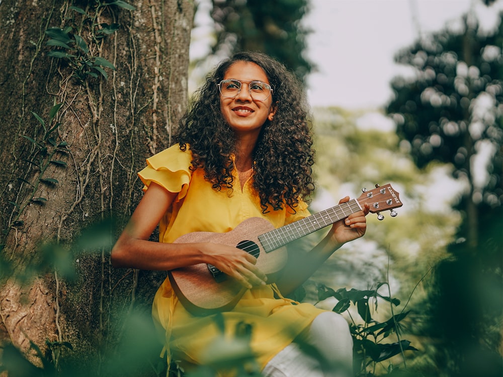 woman in yellow sleeveless dress holding brown acoustic guitar