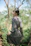 A young woman wearing pastel apricot hippie clothing, standing in a sunlit forest clearing.