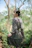 A young woman wearing pastel apricot hippie clothing, standing in a sunlit forest clearing.