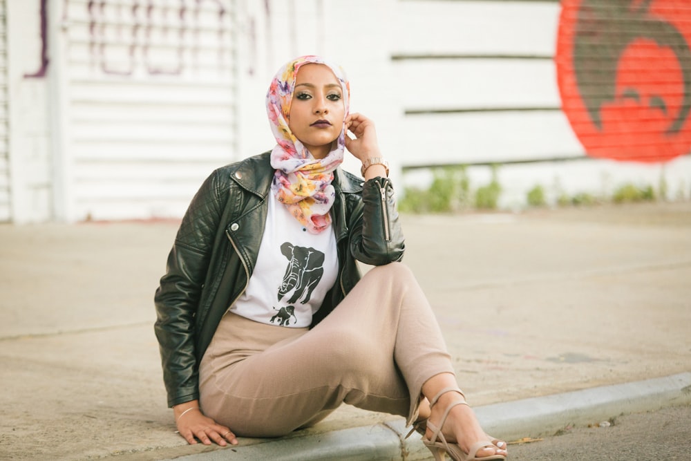 woman in black leather jacket sitting on concrete floor during daytime