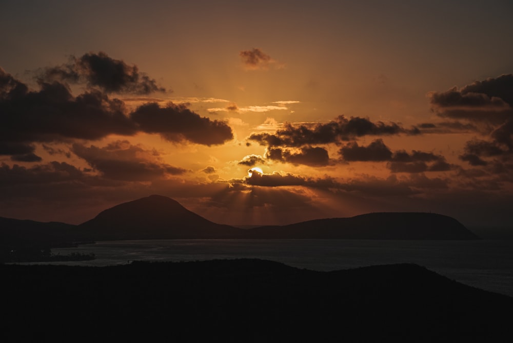 silhouette of mountain under cloudy sky during sunset