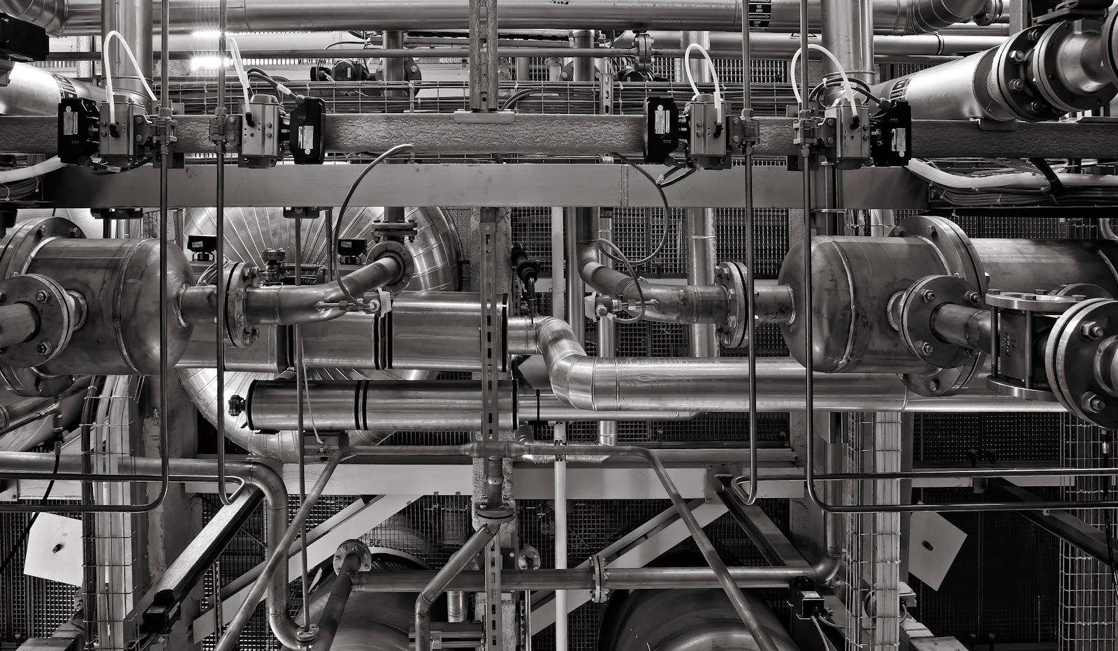 A dense run of industrial pipes and valves, unpainted metal.
