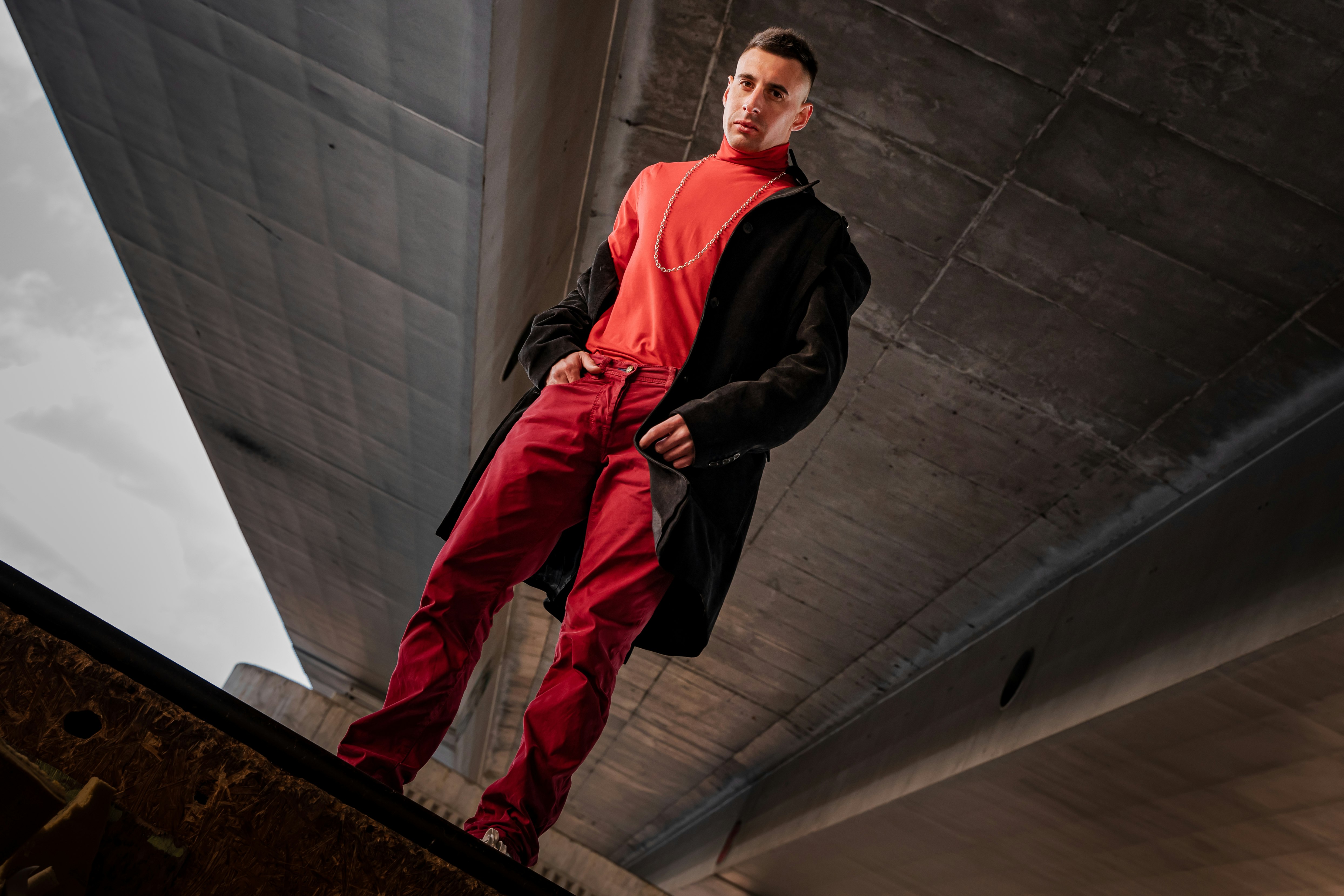 man in black jacket and orange pants sitting on concrete wall