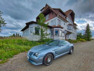 A sleek silver sedan parked beside a rustic country house.