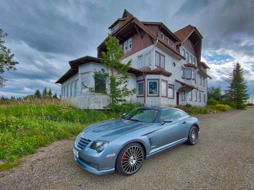 A sleek silver sedan parked beside a rustic country house.