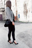 A woman in a chic black blazer paired with rugged accessories walking through an urban alley.