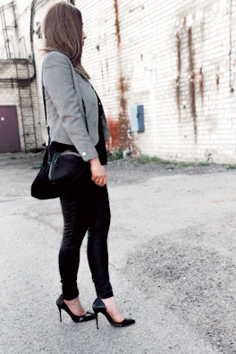 A woman in a chic black blazer paired with rugged accessories walking through an urban alley.