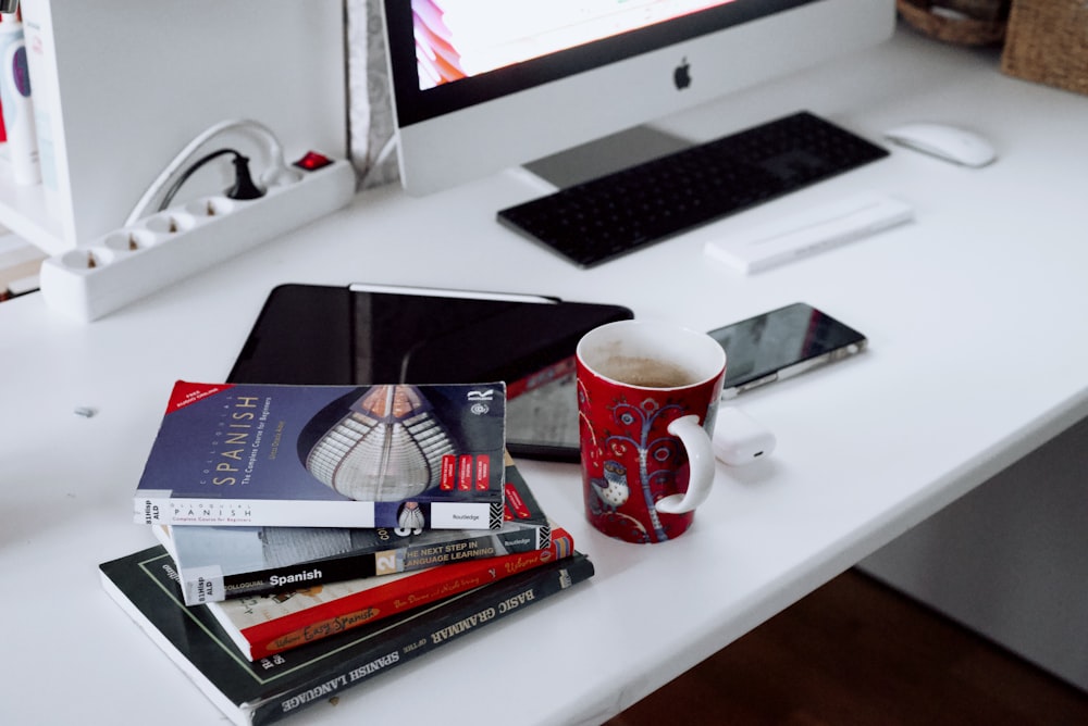 red and white ceramic mug beside silver imac