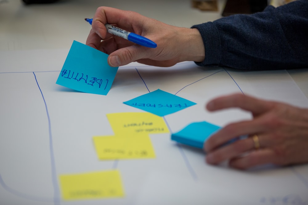 person holding blue pen writing on white paper