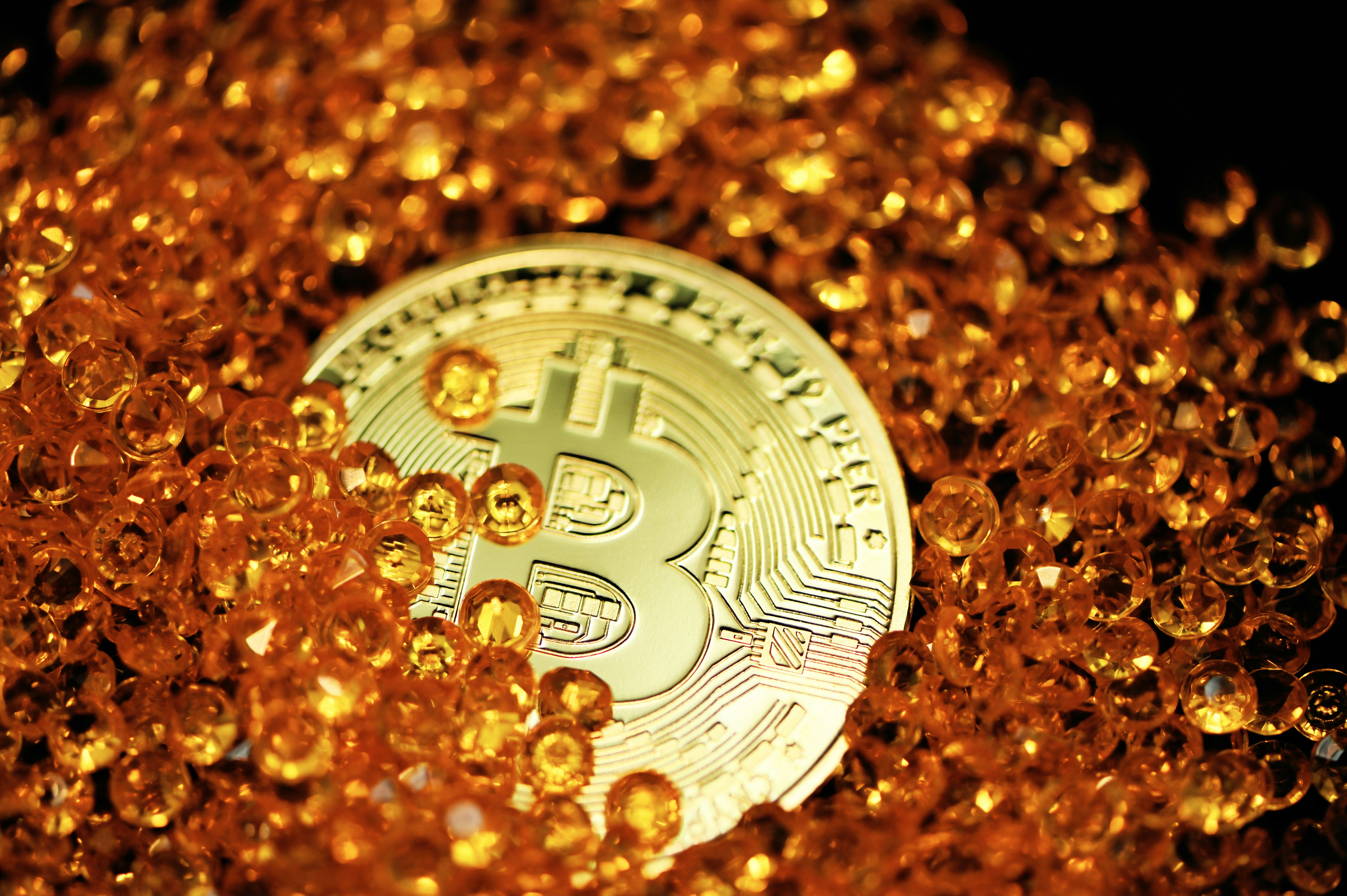 A single Bitcoin lays half buried by amber colored crystals.