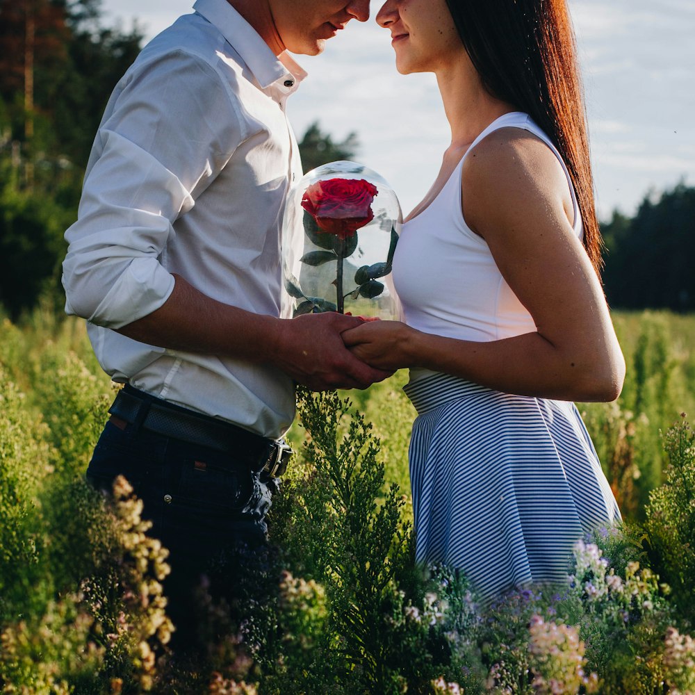 uomo in camicia bianca che tiene la rosa rossa