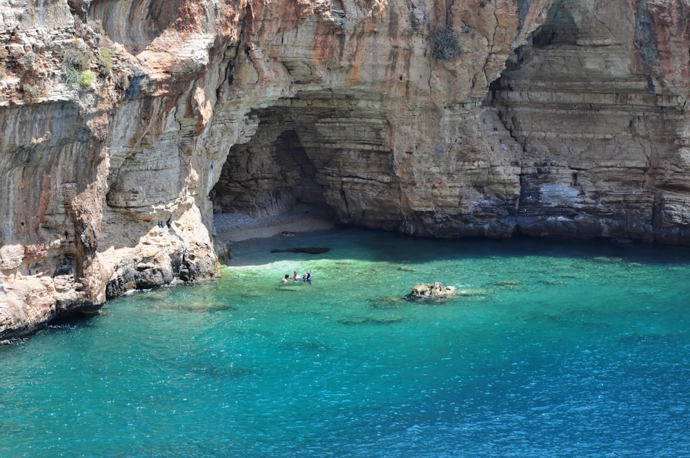 people riding on boat on sea near brown rock formation during daytime