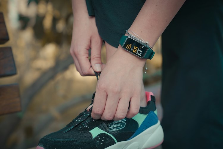 A person walking briskly along a tree-lined path wearing a fitness tracker