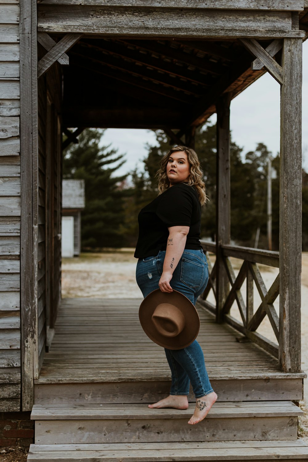 Donna in t-shirt nera e jeans blu in denim che tiene il cappello marrone