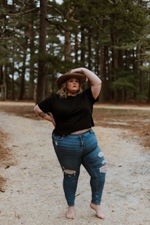 woman in black t-shirt and blue denim jeans standing on dirt road during daytime