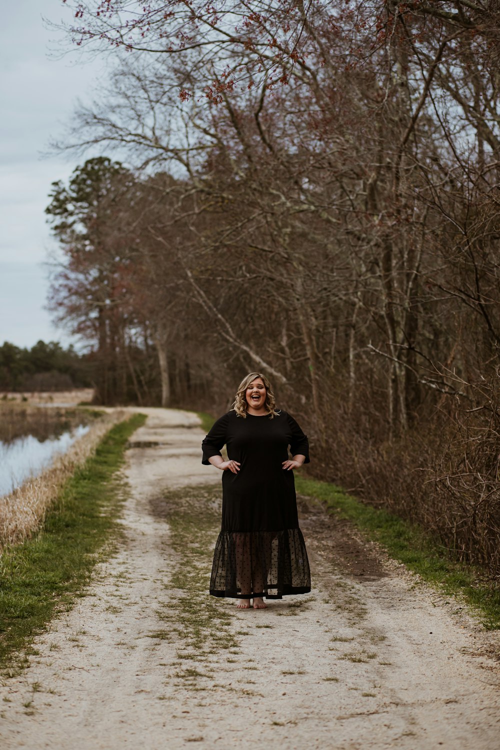 woman in black dress standing on pathway near river during daytime