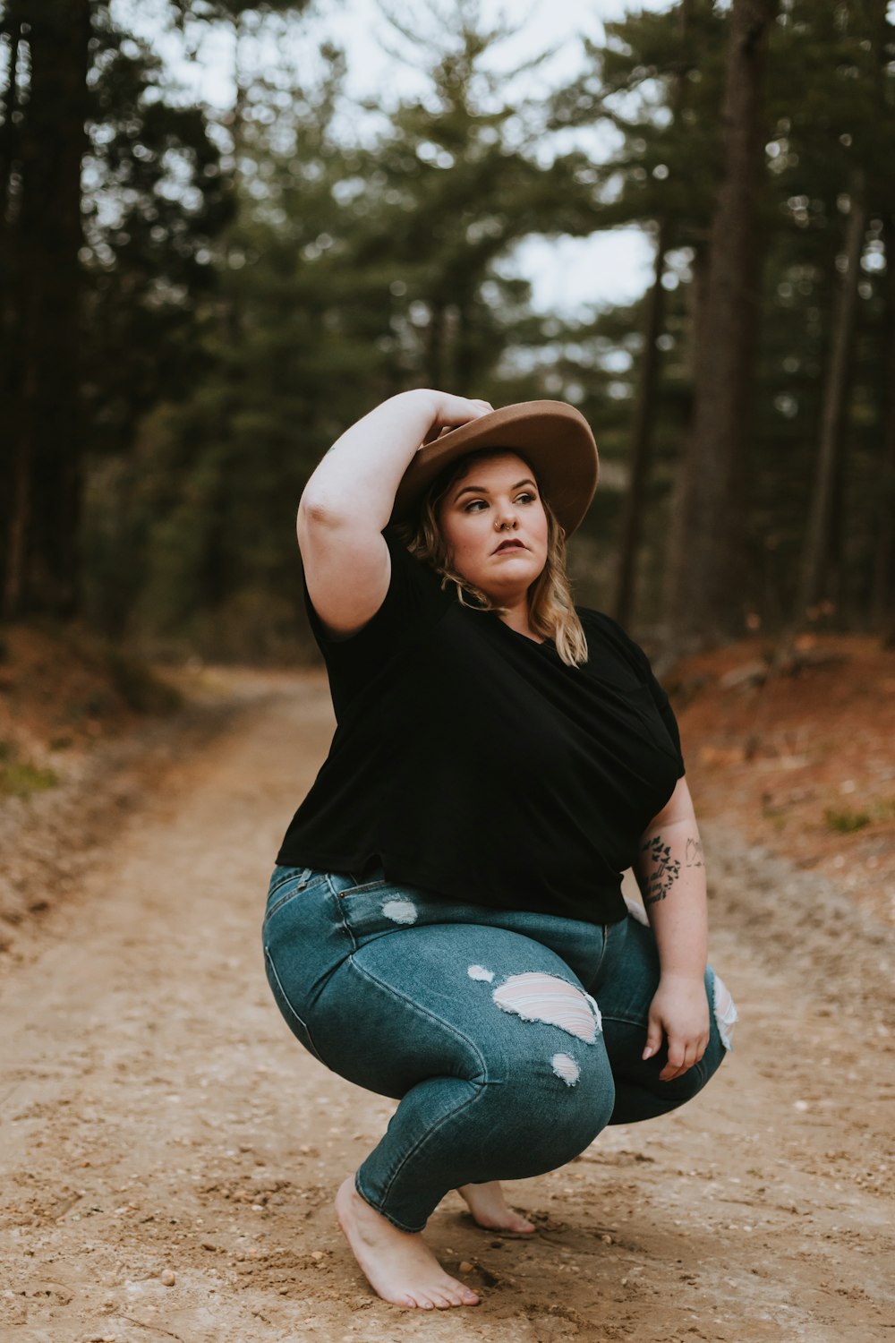 woman in black tank top and blue denim jeans sitting on brown dirt road during daytime