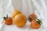 A group of ripe oranges and tangerines rests on a soft, white fabric backdrop. The fruits are vibrant orange, with some adorned with green leaves. The texture of the citrus fruits and their glossy surfaces are highlighted by the soft light.